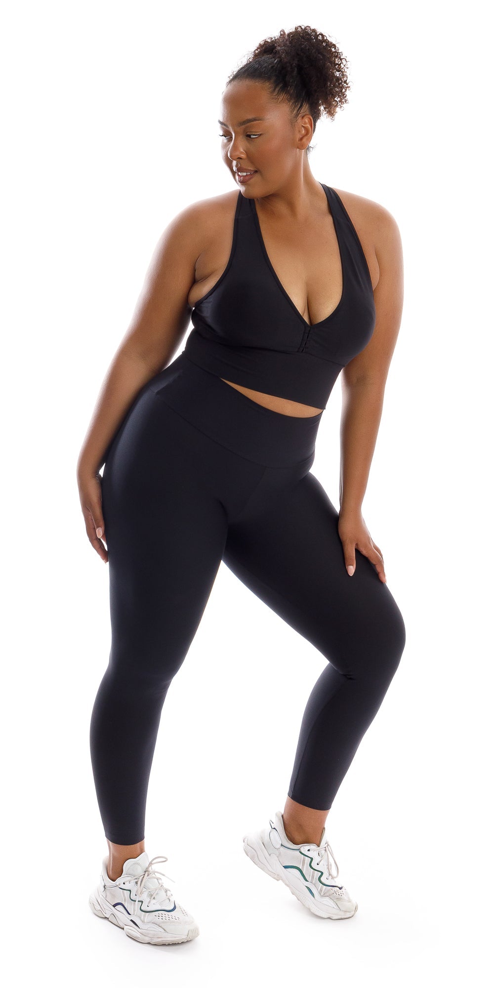 Full body front view of girl wearing black Midnight Eco Ultra High Waist Leggings and matching bra leaning on left bent knee